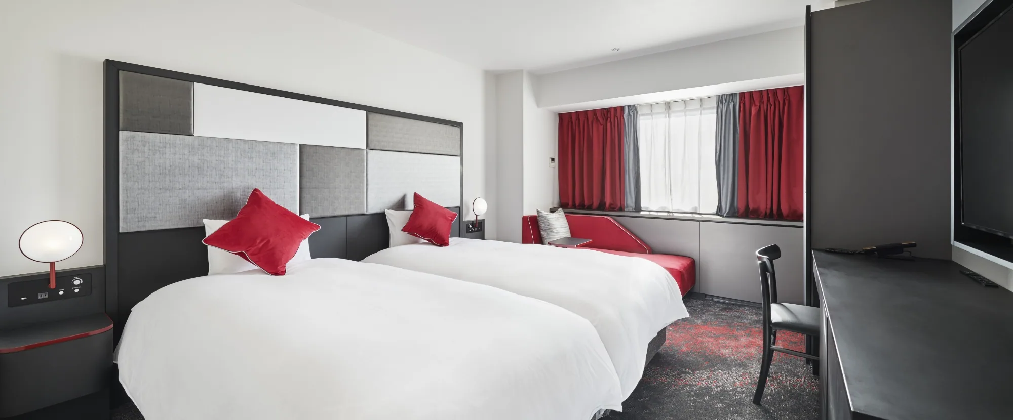 Helles Hotelzimmer mit zwei Betten und roten Akzenten
